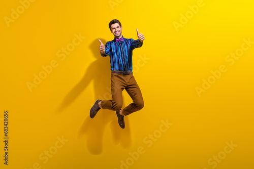 Full body photo of satisfied funky man wear bow tie stylish shirt jumping showing thumbs up to you isolated on yellow color background © deagreez