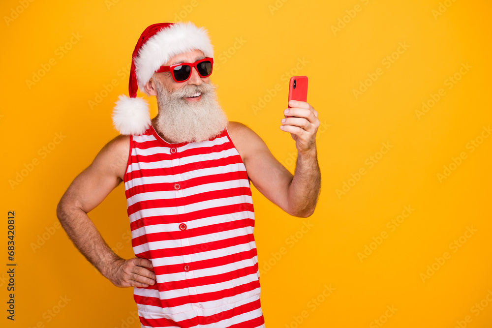 Photo of funky cheerful senior guy christmas swimwear hat glasses texting twitter telegram empty space isolated yellow color background Photo of funky cheerful senior guy christmas swimwear hat glasses texting twitter telegram empty space isolated yellow color background