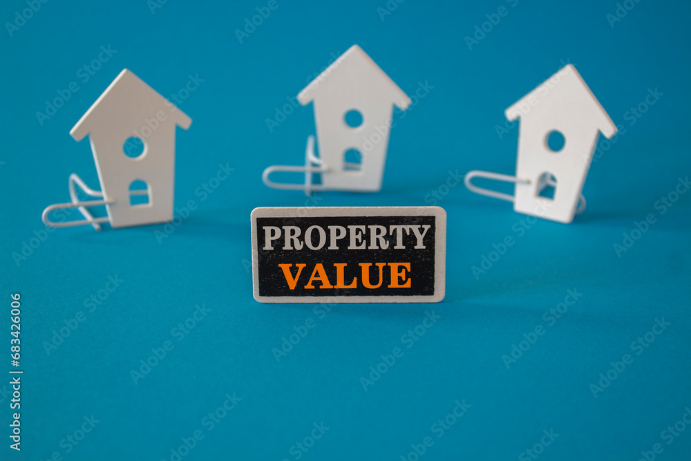 Property value symbol. Wooden houses sits next to a wooden black board with the word Property value . Beautiful blue background. Business property value concept. Copy space. Property value symbol. Wooden houses sits next to a wooden black board with the word Property value . Beautiful blue background. Business property value concept. Copy space.