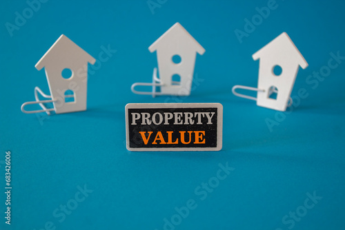 Property value symbol. Wooden houses sits next to a wooden black board with the word Property value . Beautiful blue background. Business property value concept. Copy space.