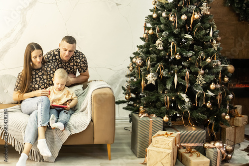 a family sits on the sofa near a beautifully decorated New Year tree. dad, mom and little son in the living room decorated for Christmas. Christmas.  New Year © Ольга Листратова