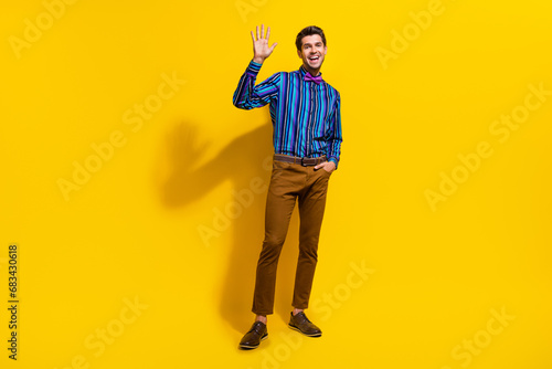 Full body photo of good mood pleasant man with bristle wear vintage bow tie waving palm say hello isolated on yellow color background © deagreez
