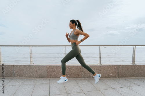 beautiful slender brunette, sportswear and a fitness bracelet runs along the embankment, does sports, develops endurance. Asian young woman doing an outdoor workout. Active people, healthy lifestyle