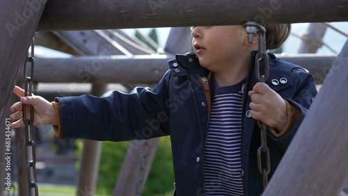 Focused Child playing at playground structure, crossing bridge and holding into metal chains standing on wooden steps
