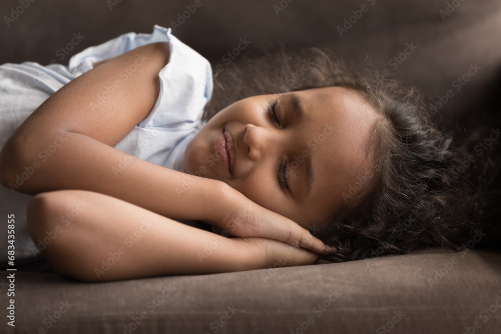 Obraz premium Close up shot beautiful little Indian girl put folded palms under head sleeps on sofa at home, enjoy healthy daytime nap looks serene, take break, rest alone indoor. Relaxation, fatigue relief concept