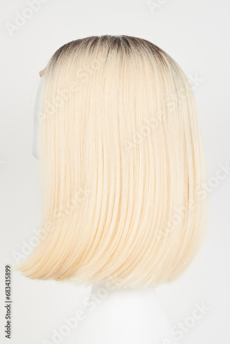 Natural looking blonde fair wig on white mannequin head. Middle length hair cut on the plastic wig holder isolated on white background, side view.
