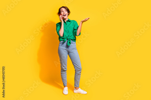 Full length photo of shiny excited girl dressed green shirt talking apple iphone samsung device empty space isolated yellow color background
