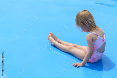 One little blond girl is sitting in the blue pool. A sadness of one little girl in the middle of the summer