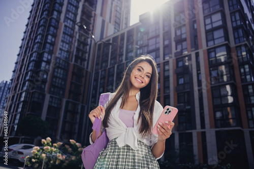 Portrait of lovely cheerful person toothy smile hold bag smart phone texting sunny weather city buildings outdoors