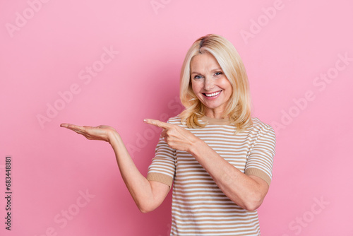 Photo of cheerful person with blond hairstyle dressed striped t-shirt directing at empty space on hand isolated on pink color background