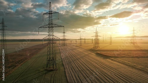 Energy power transmission towers in field landscape at sunrise aerial shot. Electricity pylon with nature scenery and cloudscape at morning