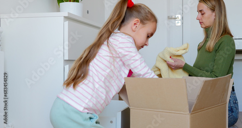 Little girl with mother putting clothes to drawer in bedroom after moving
