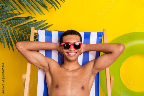 Photo of positive charming shirtless man dark glasses having rest lounge chair arms behind head isolated yellow color background