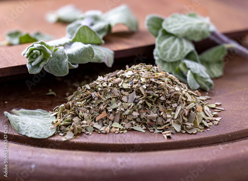 Chopped dried oregano and green oregano leaves on the wooden board