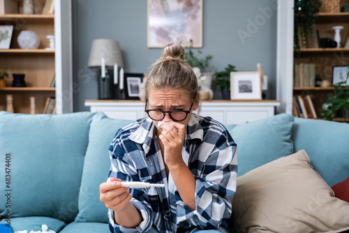Single sad woman complaining holding a pregnancy test sitting on a couch in the living room at home, Stressed female, Positive or negative medical test pregnant or not. photo