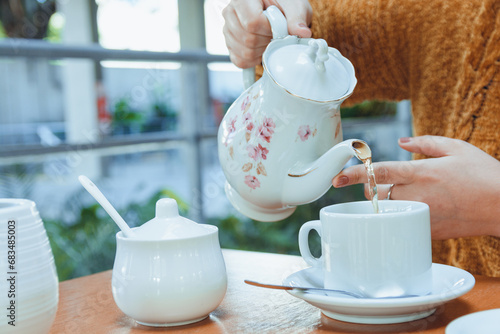 close-up of unrecognizable woman with porcelain teapot pouring tea into porcelain cup on the table