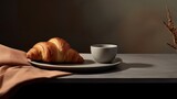  a plate with a croissant on it next to a cup of coffee and a plant on a table.