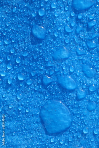 Large water droplets on blue polyethylene blue tarpaulin in daylight Vertical