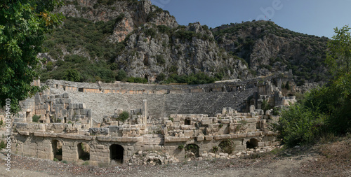 Glued wide panorama of amphitheatre ancient ruins: carved windows, passages, arches. Remains of ancient Lycia civilization, Myra dead antique city in Turkey. Mountain landscape in the background