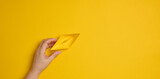 Female hand hold a blue paper boat on a yellow background. Mentoring and support concept