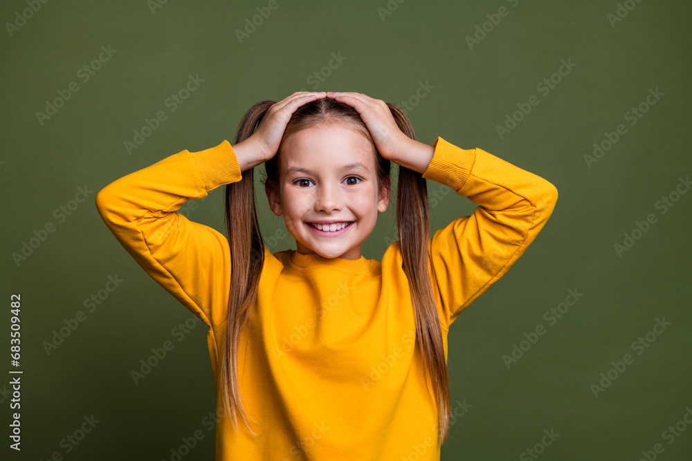 Portrait of impressed small kid with tails hairstyle dressed yellow sweatshirt hold arms on head isolated on khaki color background Portrait of impressed small kid with tails hairstyle dressed yellow sweatshirt hold arms on head isolated on khaki color background