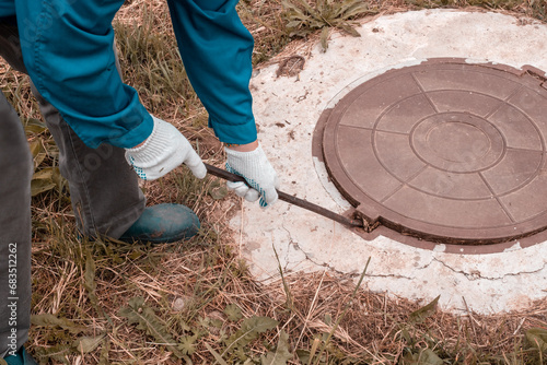 A worker opens a well hatch with a pry bar. Troubleshooting, checking septic tanks photo