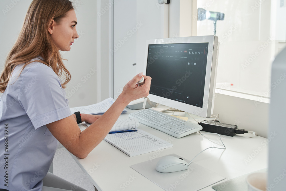 Lady doctor sitting computer workplace and holding special device for making x ray