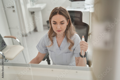 Lady doctor sitting computer workplace and holding special device for making x ray