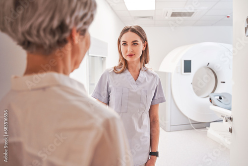 Lady radiographer talking with female patient after operating CT scanner at hospital