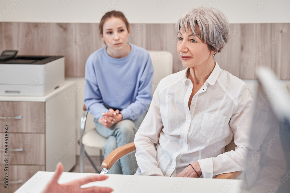 Obraz premium Positive grandmother sitting at the table and smiling to her doctor during medical check up