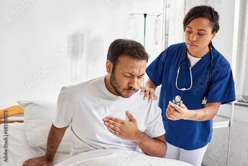 young african american nurse giving asthma inhaler to her ill indian patient in his ward, healthcare