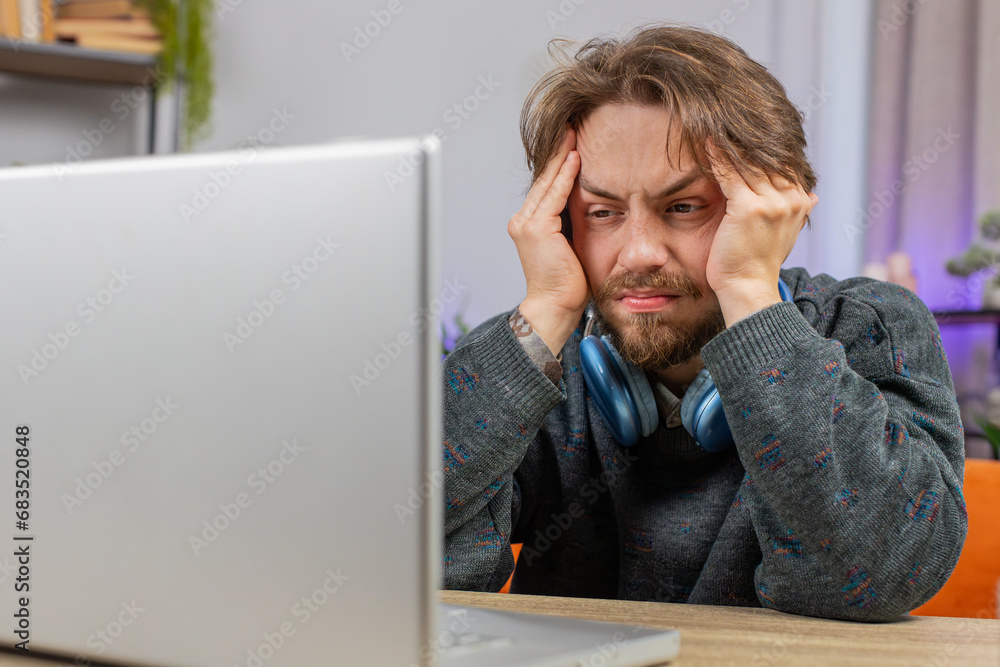 Tired Caucasian man freelancer use laptop, suffering from headache problem tension, migraine, stress at home desk. Guy works on notebook, sends email messages, makes online purchases, watching movies Tired Caucasian man freelancer use laptop, suffering from headache problem tension, migraine, stress at home desk. Guy works on notebook, sends email messages, makes online purchases, watching movies