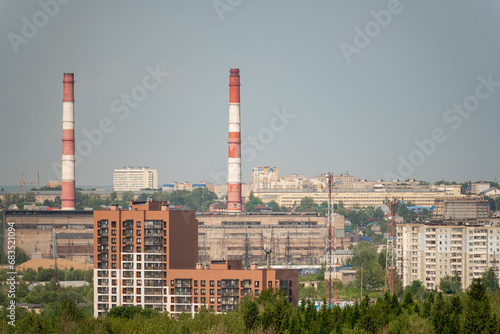 Tall industrial pipes rise above residential buildings against the blue sky..