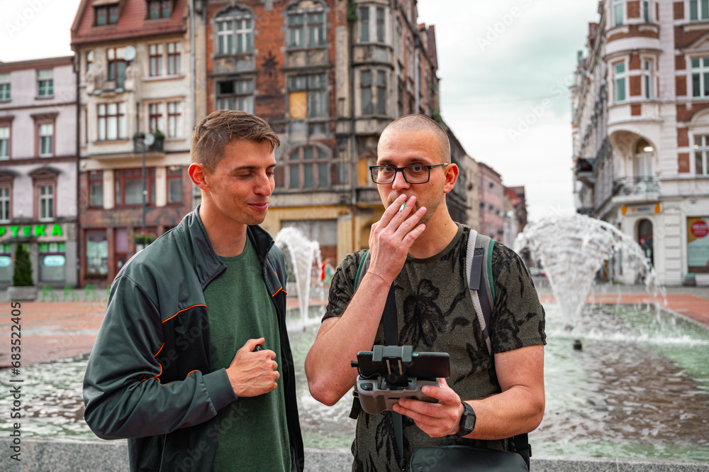 Two brothers operating a drone in an old city. One man smoking a cigarette.