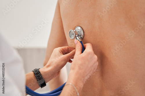 Close up of general practitioner sitting behind the back of patient and using stethoscope