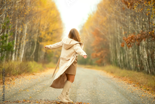 A girl in a light coat runs away into the distance along a country road in the autumn forest. © Ann Stryzhekin
