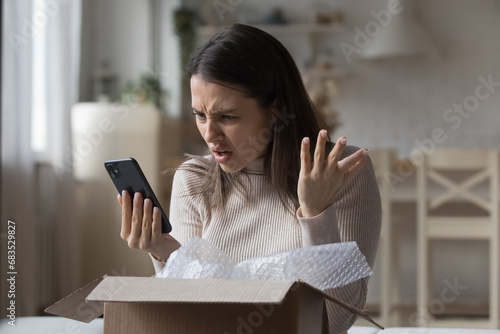 Dissatisfied woman, internet store client got damaged items, receive wrong parcel, make claim send negative feedback use cellphone feels angry. E-commerce mobile app, bad e-shopping experience concept photo