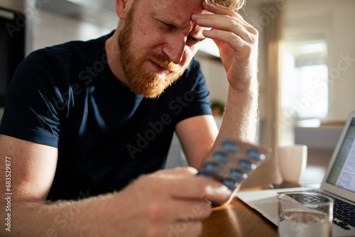 Bearded man holding medication packaging at home