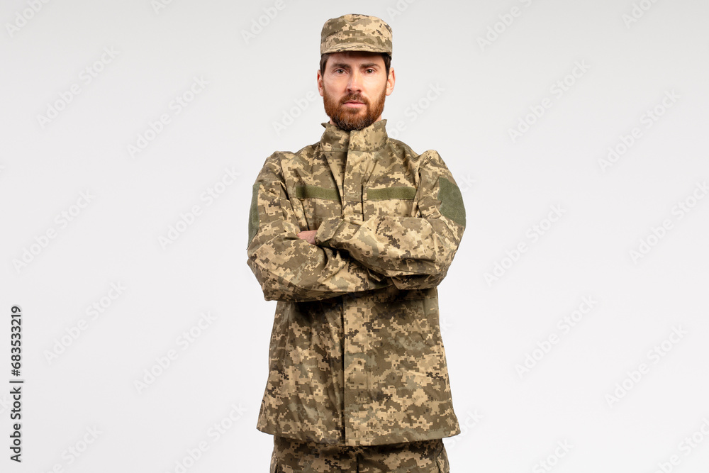 Handsome serious bearded man, professional soldier wearing camouflage military uniform holding arms crossed isolated on white background Handsome serious bearded man, professional soldier wearing camouflage military uniform holding arms crossed isolated on white background