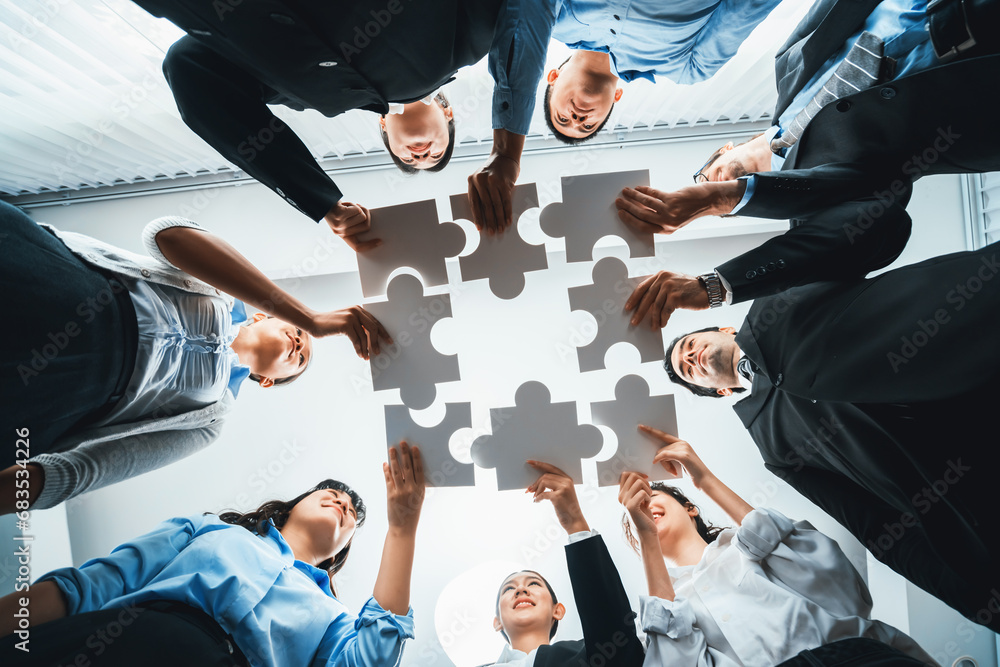 Multiethnic business people holding jigsaw pieces and merge them together as effective solution solving teamwork, shared vision and common goal combining diverse talent. Below view. Habiliment - obrazy, fototapety, plakaty 