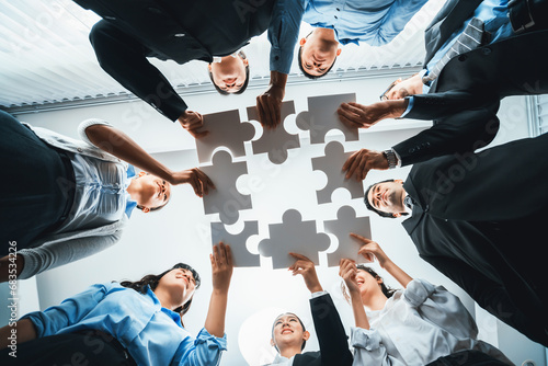 Multiethnic business people holding jigsaw pieces and merge them together as effective solution solving teamwork, shared vision and common goal combining diverse talent. Below view. Habiliment photo