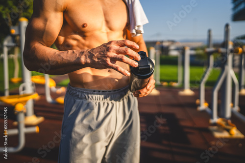 One caucasian man young male athlete take a brake during outdoor training in the park outdoor gym hold supplement shaker in hand happy confident strong copy space photo