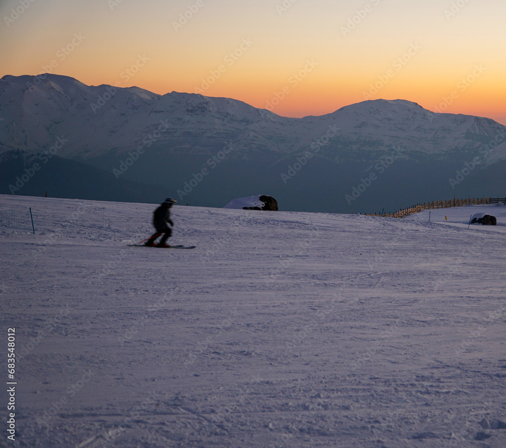 At sunset, a ski slope and a person skiing create a picturesque winter scene.