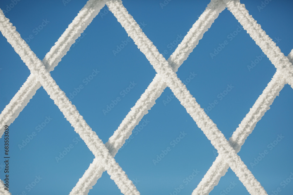Frozen grate in winter. lattice with frost on the background of the blue sky. grid covered with snow, mesh covered with frost. Metal grating in the frost. White fluffy snow formed on the trellis.