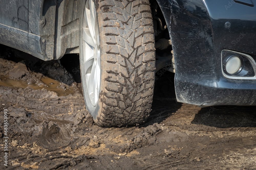 Winter car tires are covered with mud, the car is in the mud. Tough road conditions highlight the need to use the right tires to drive safely in challenging conditions