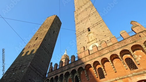 Perspective bottom view of Two Towers of Bologna, symbol of city in blue sky, Italy. Asinelli tower and Garisenda tower in historic downtown with clock tower of Bologna city in Porta Ravegnana square. photo