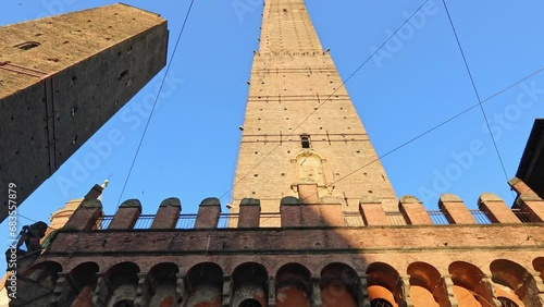 Looking up from below, Two Towers of Bologna, emblematic of city against a blue sky in Italy. Asinelli and Garisenda towers stand tall in historic downtown by the clock tower in Porta Ravegnana square photo