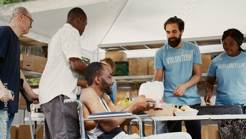 Charity organization shows devotion to fighting hunger and poverty by handing out hot meals to the underprivileged. Warm food is provided by volunteers to the male african american wheelchair user.