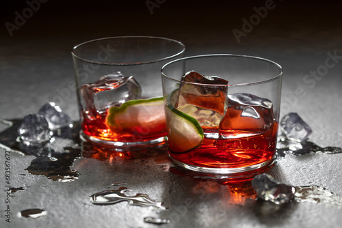 2 backlit, dark half empty cocktails with ice