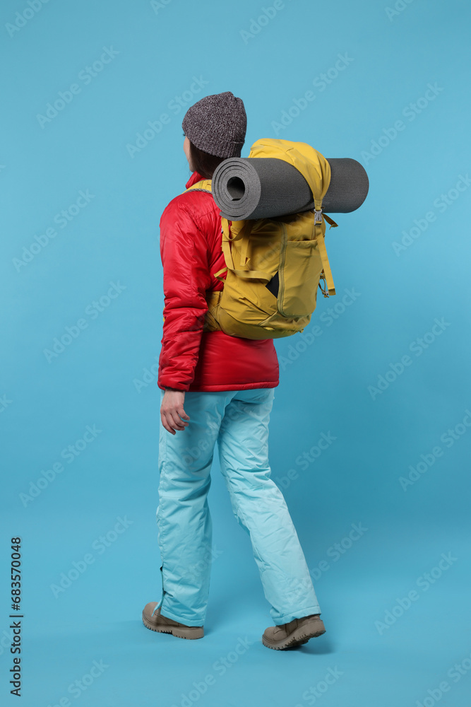 Woman with backpack walking on light blue background. Active tourism
